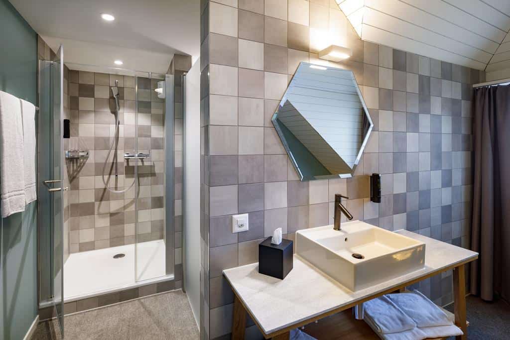 Compact tiled bathroom with glass shower and geometric mirror