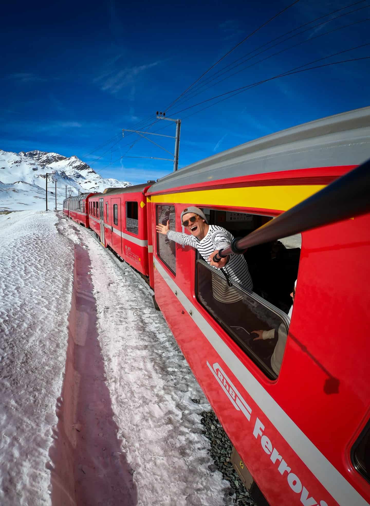 Swiss Travel Pass: All You Need To Know (2025 Guide) 9 Man leaning out of scenic red Swiss train.