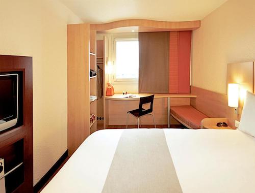 Compact budget hotel room with built-in desk and closet