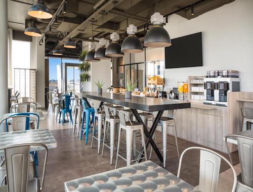 Industrial-style hotel breakfast area with long tables and metal chairs
