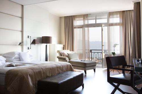 Stylish hotel room with beige tones, a cozy armchair, and a balcony overlooking the lake