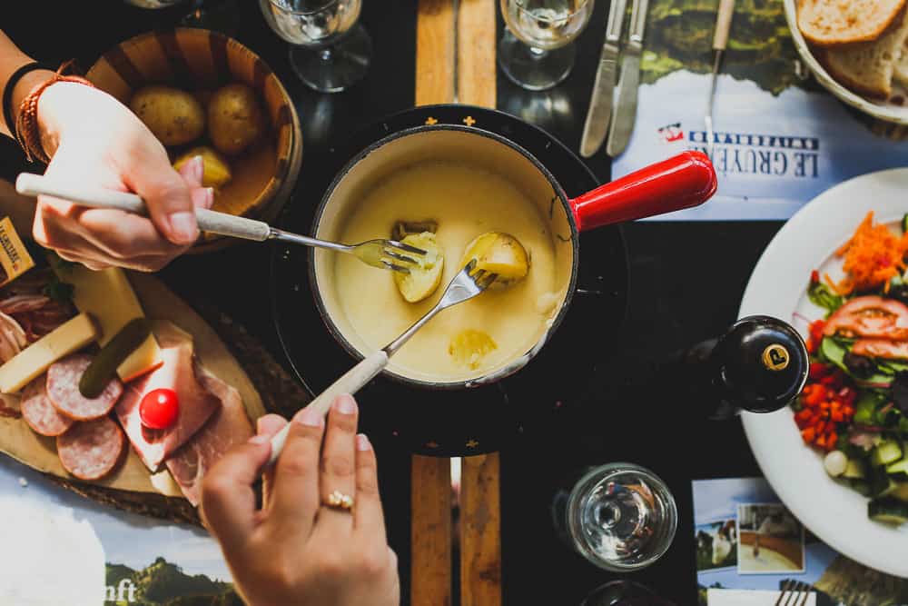 Close-up of people dipping bread and potatoes into a cheese fondue