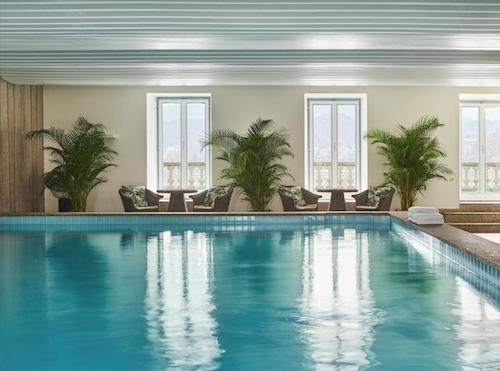 Indoor swimming pool with windows and tropical plants.