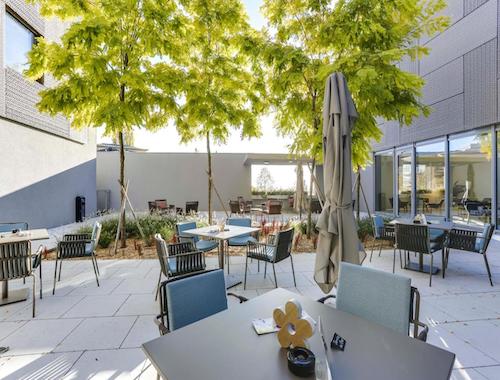 Outdoor hotel terrace with shaded tables, chairs, and small trees