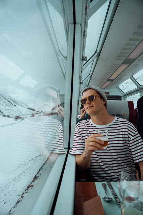 The BEST 8 Day Switzerland Itinerary For First-Timers (2025) 42 Man drinking beer while riding a scenic train through snowy landscapes