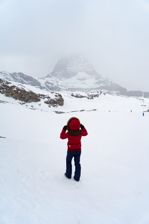 The BEST 8 Day Switzerland Itinerary For First-Timers (2025) 37 Person standing in front of a snow-covered mountain with fog covering the peak